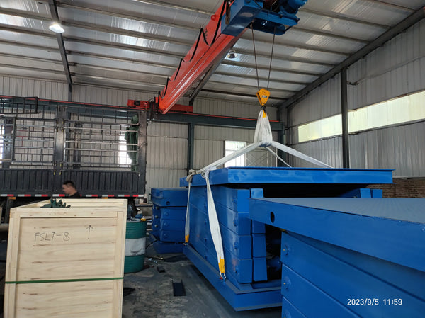 Blue fixed scissor lift suspended from an overhead crane with white lifting slings in the BEACON Industries workshop.